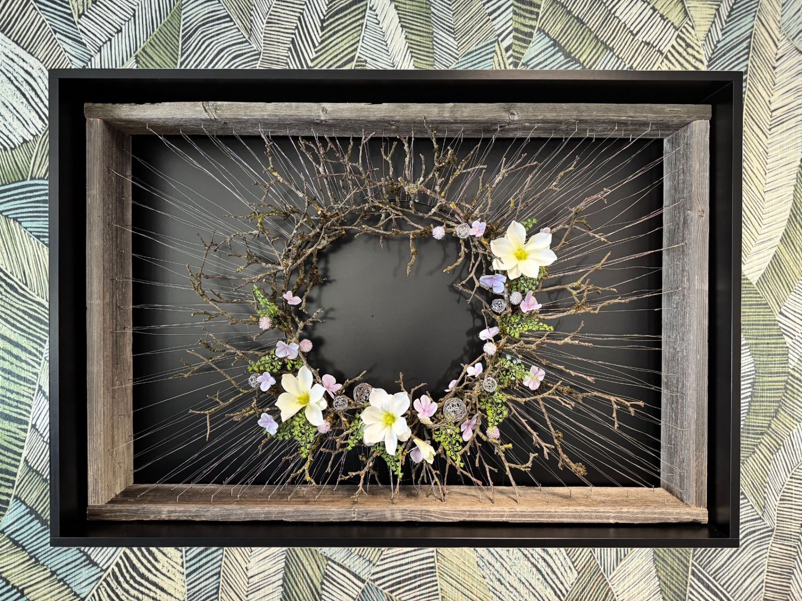 Botanisches Wandobjekt mit Blüten und Ästen in einem Holzrahmen